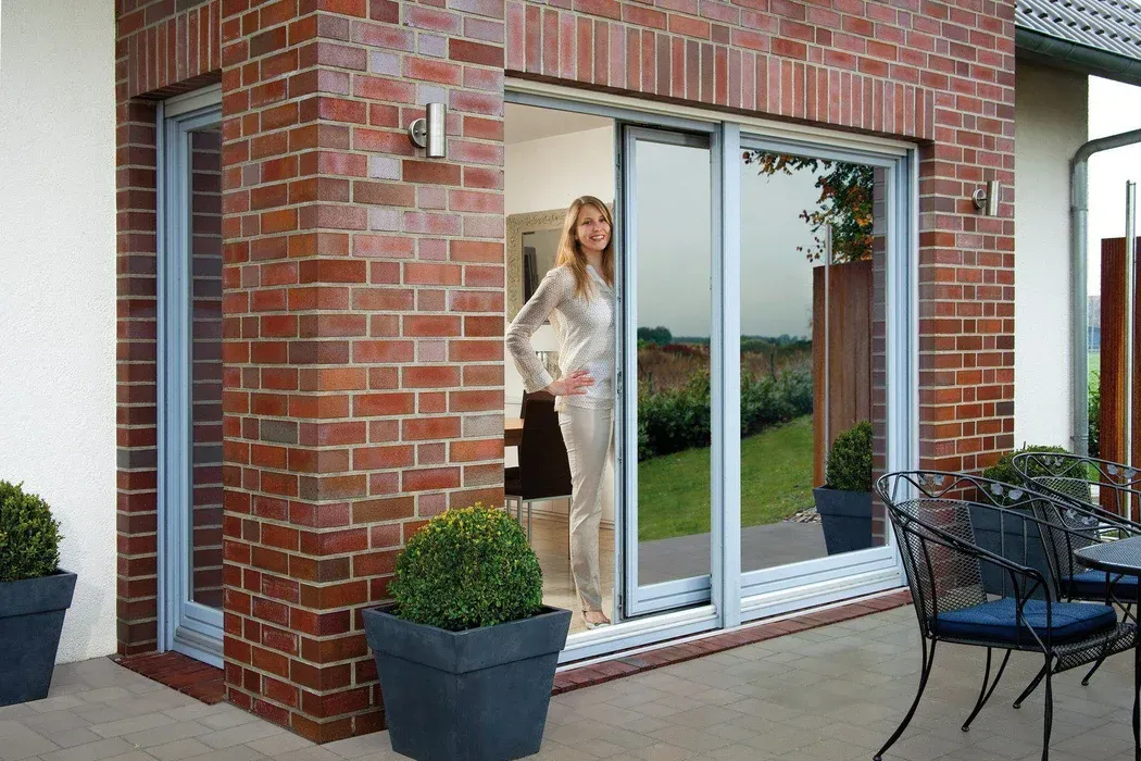 Woman standing in sliding glass door, brick wall, potted plants, outdoor patio.