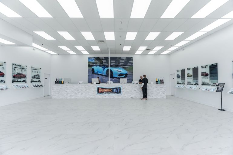 Bright, modern retail space. A person stands at a counter in front of a large screen. Walls have display cases with product images.