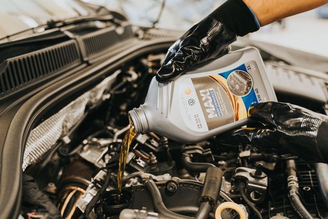 Gloved hands pour motor oil into a car engine under the hood