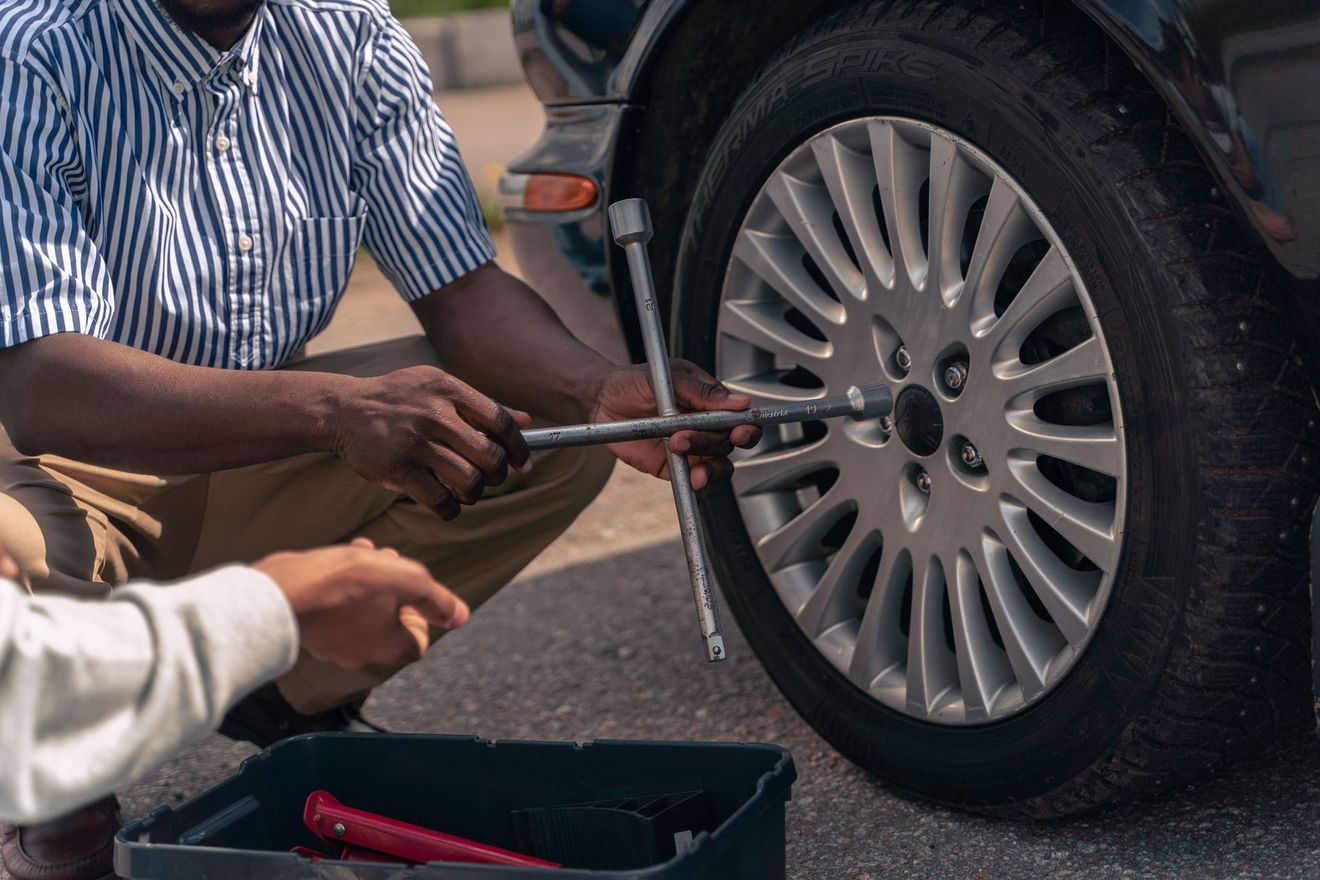 Two people using a lug wrench to tighten wheel nuts on a car tire outdoors