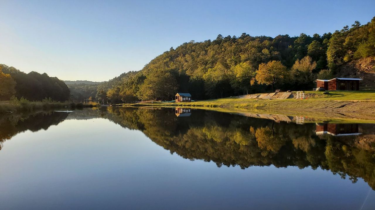 A lake surrounded by trees and mountains with a reflection of trees in the water.