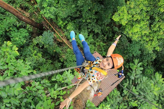A woman is flying through the air on a rope in the jungle.