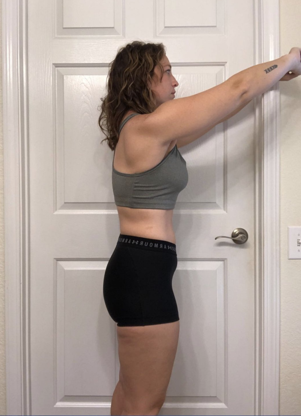 A woman in a sports bra and shorts is standing in front of a door.