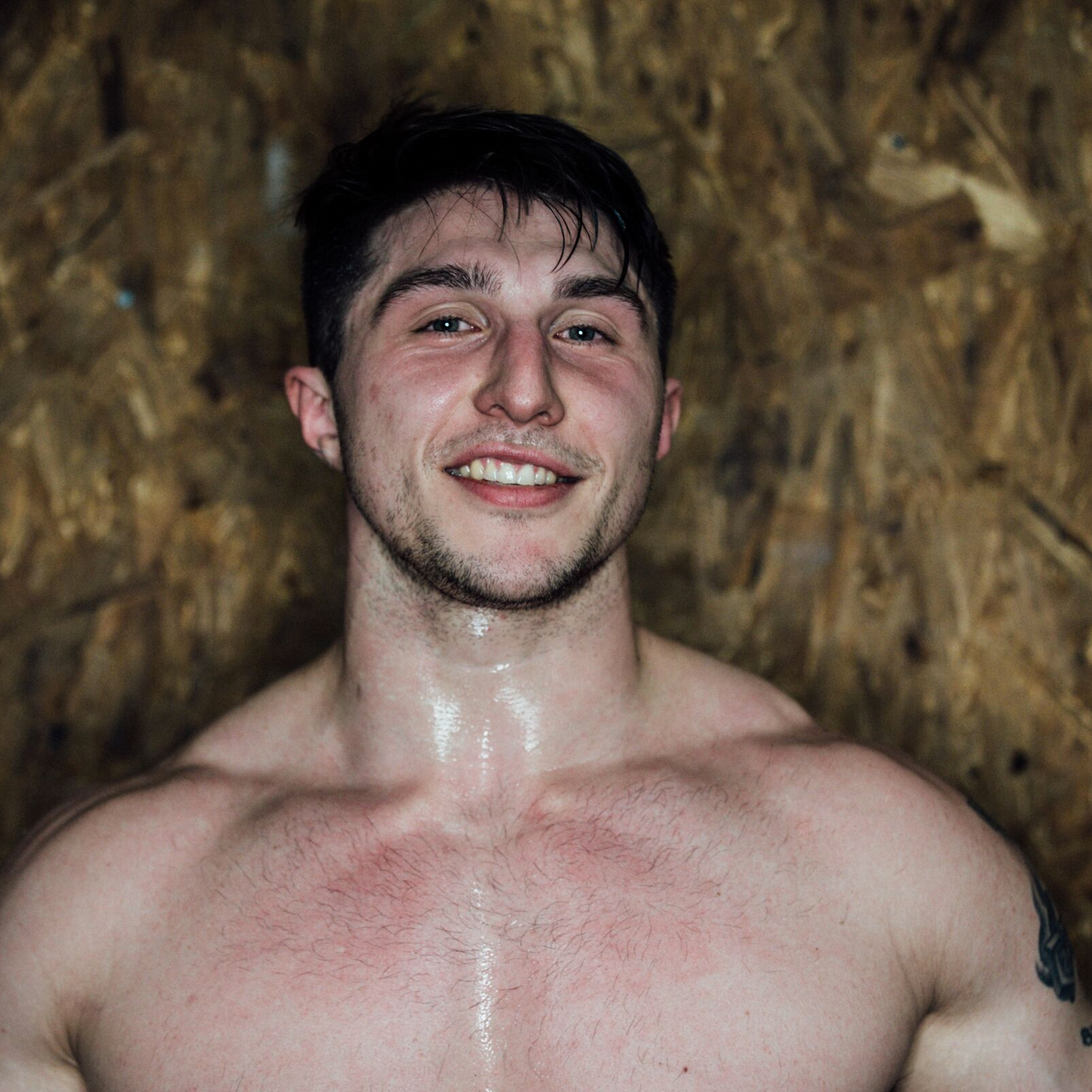 A shirtless man with a tattoo on his arm is smiling for the camera.