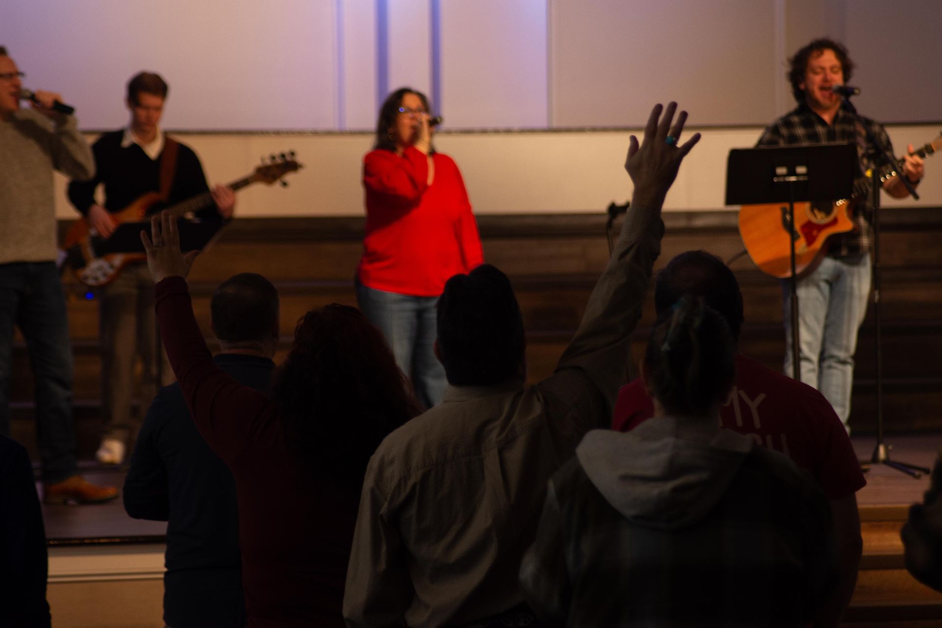 People singing in a church. Choir in center, cross on wall, screen and pews visible.