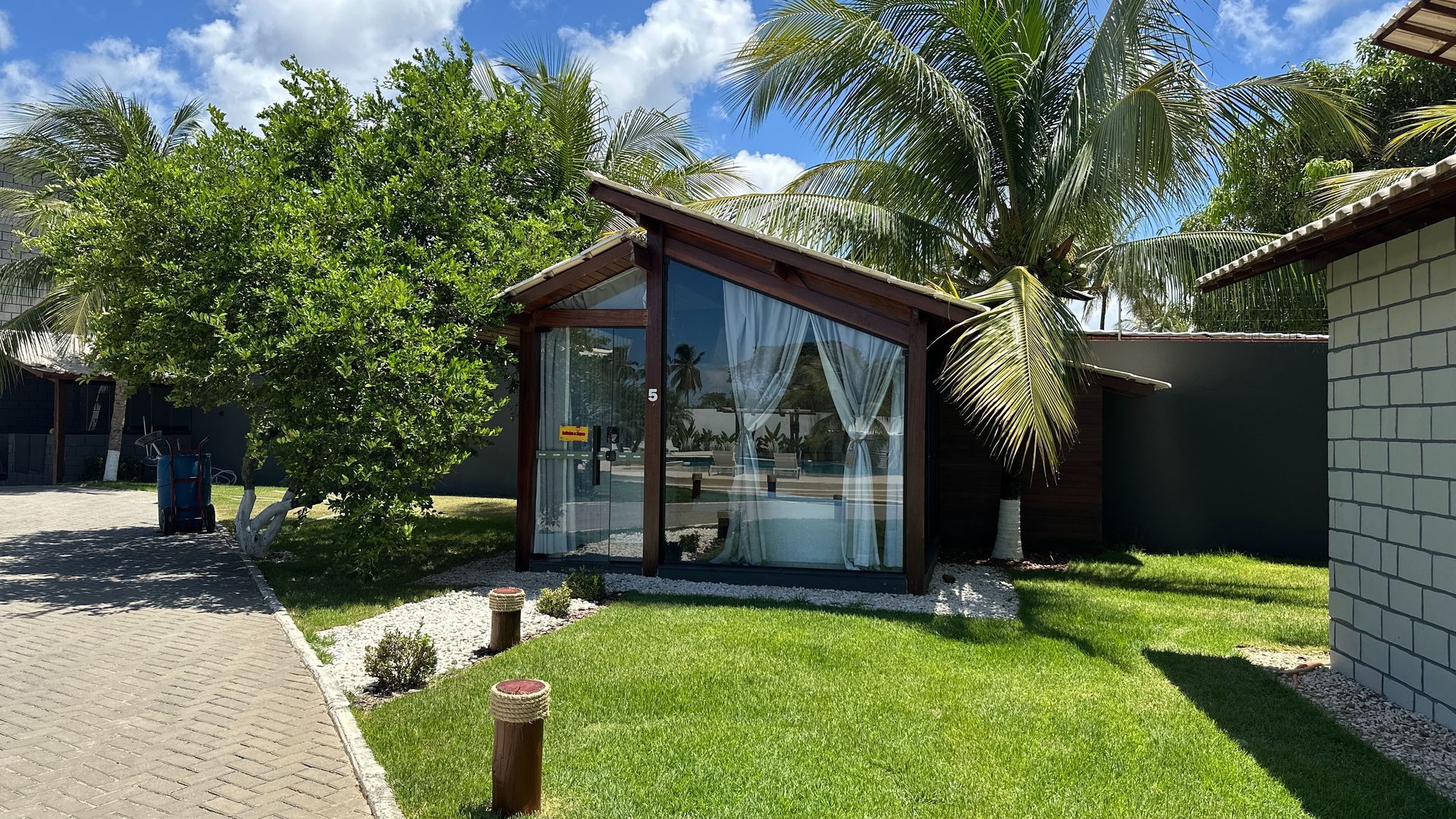 Uma pequena casa com muitas janelas cercada por árvores e grama.