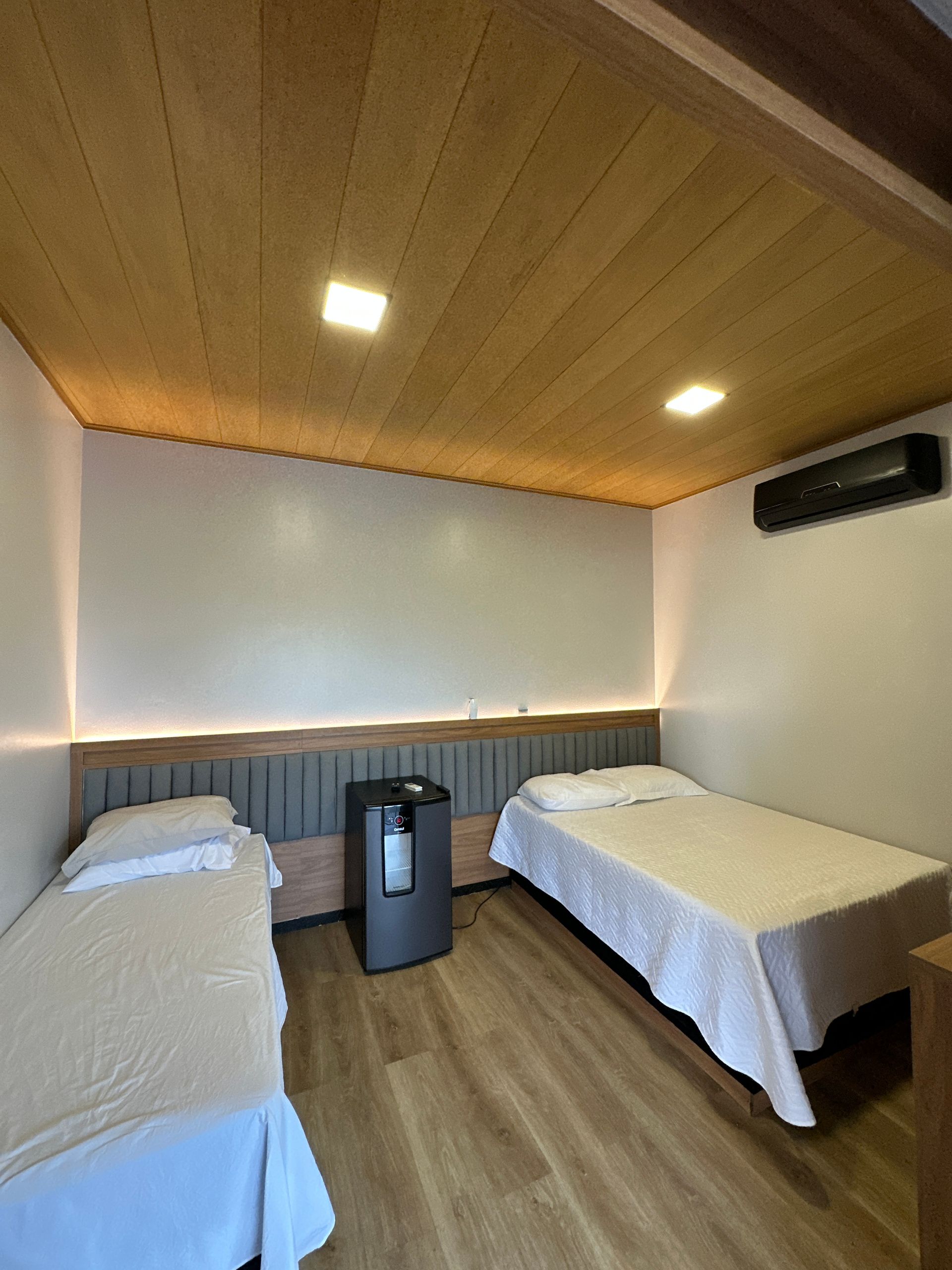 Um quarto com duas camas e uma geladeira.