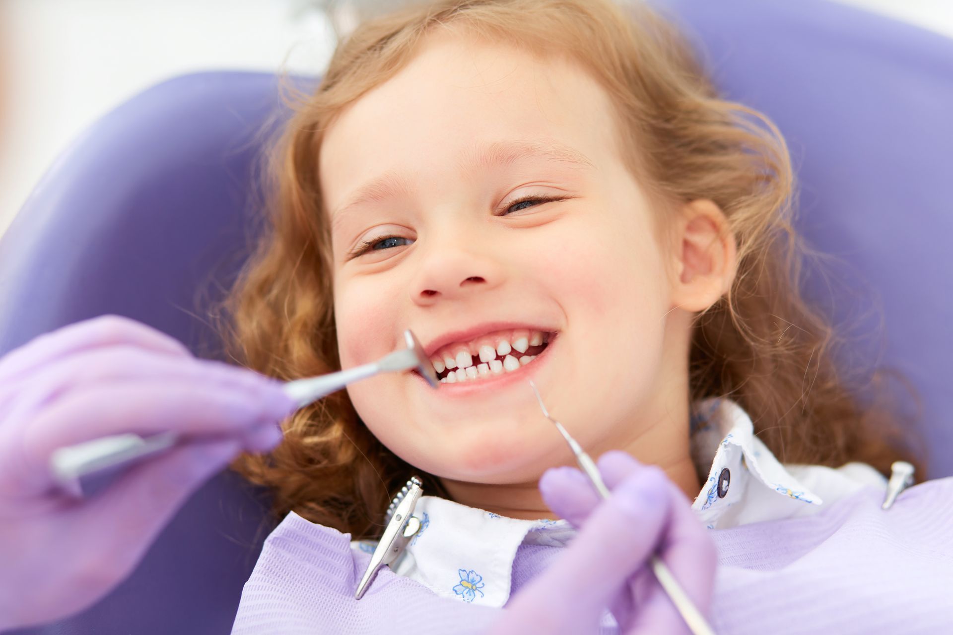 A young girl smiles happily while sitting in a pediatric dentist chair, ready for her appointment.