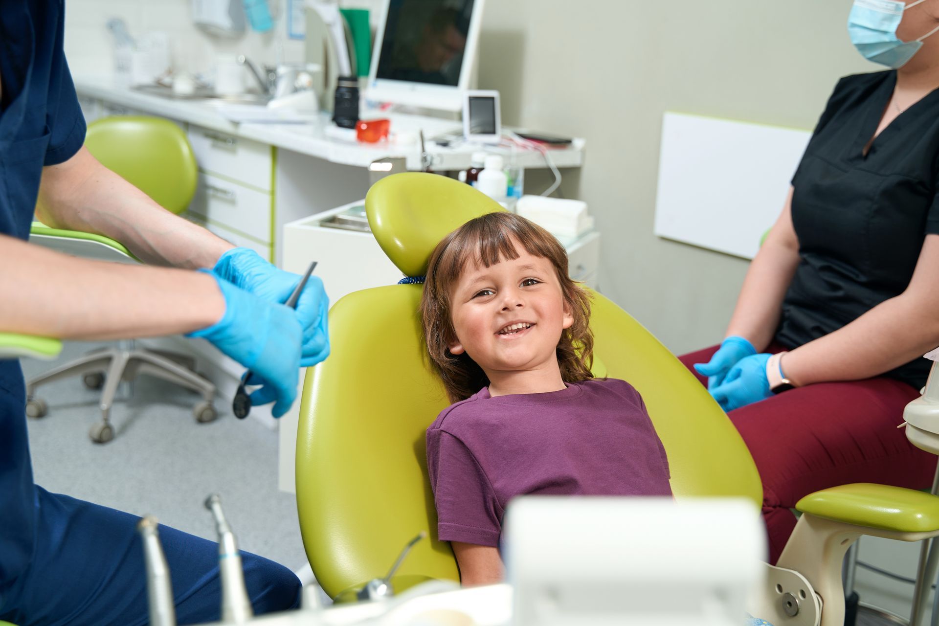 Child sitting in dental chair while pediatric dentist prepares tools for a routine checkup.