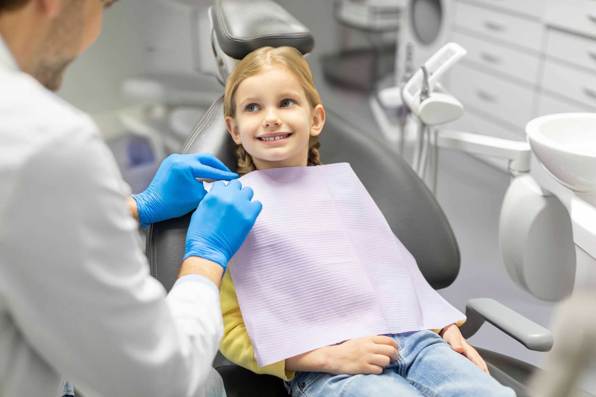 A dentist is preparing to conduct a procedure or checkup on a little female patient.