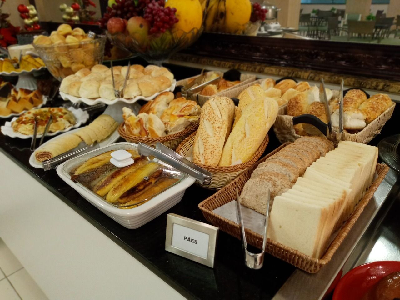 Uma mesa de bufê com diversos tipos de pães, doces e frutas.