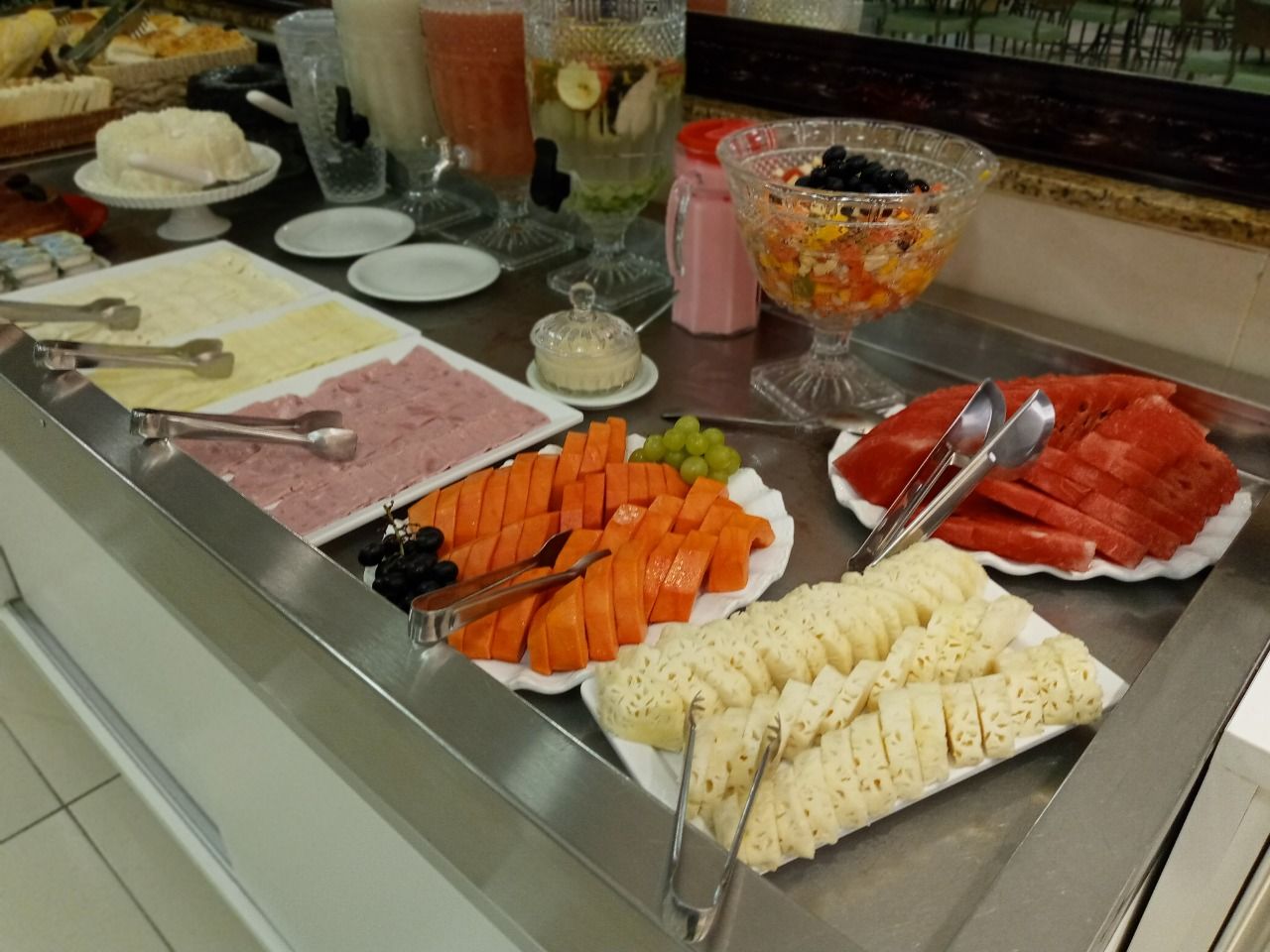 Buffet de café da manhã com frutas, queijos, sucos e outros alimentos.