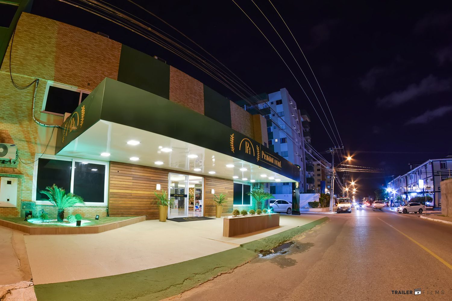 Entrada do hotel à noite, com toldo verde, porta iluminada e vista para a rua.
