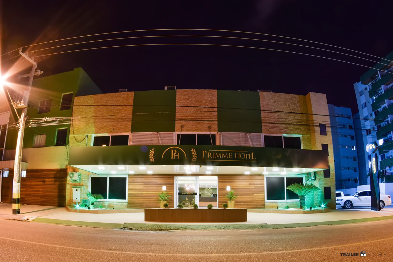 Exterior do hotel à noite, com letreiro iluminado e postes de luz, design moderno, céu escuro.