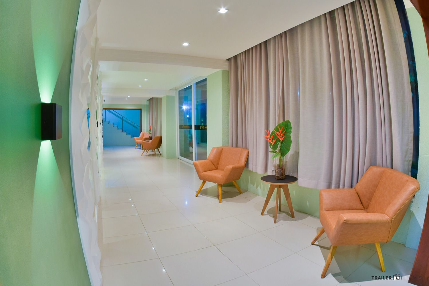 Corredor bem iluminado com poltronas cor de pêssego, cortinas bege e paredes verdes.