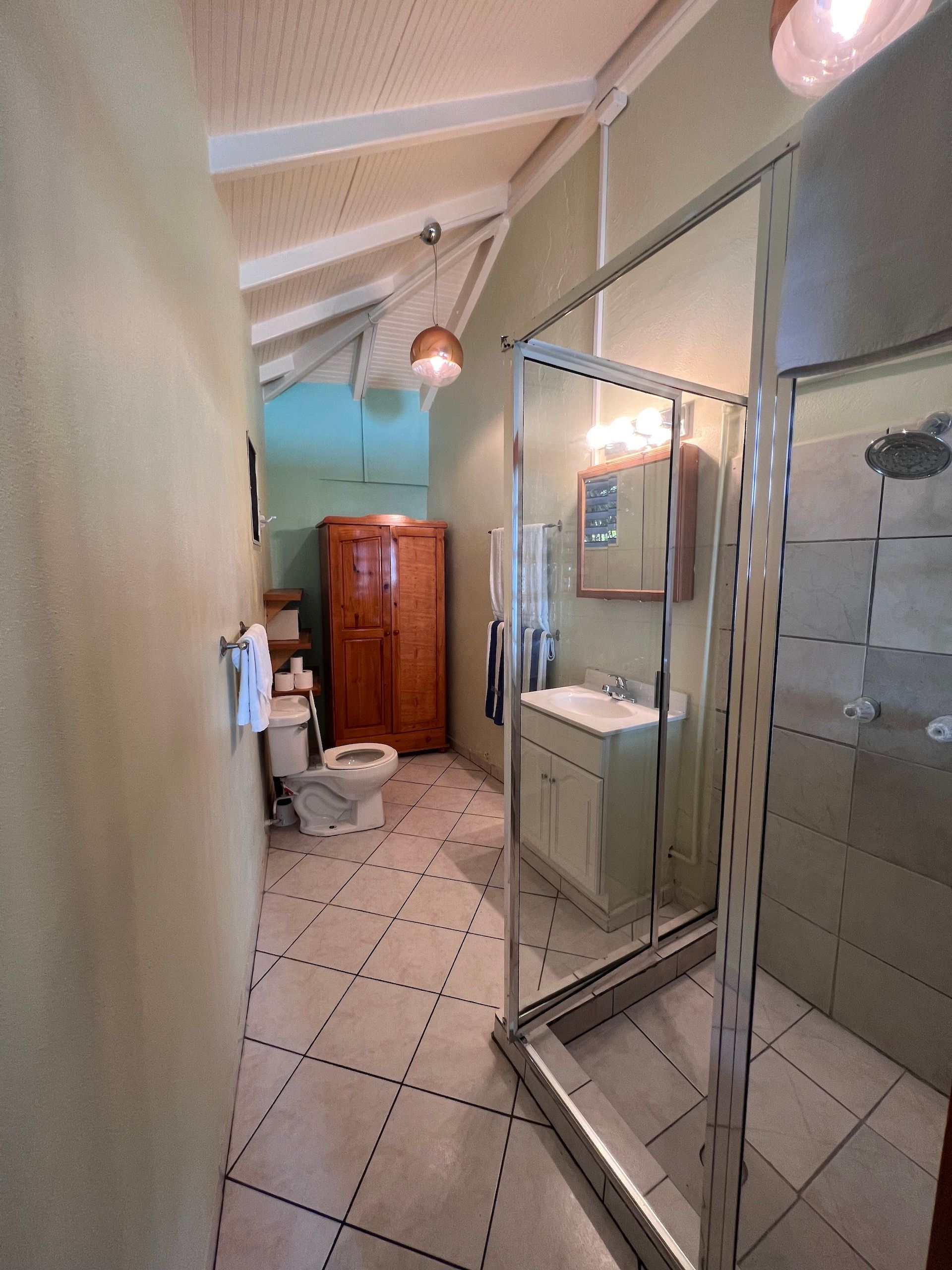 Bathroom with shower, toilet, sink, and wooden cabinet; beige, white, and light green colors.