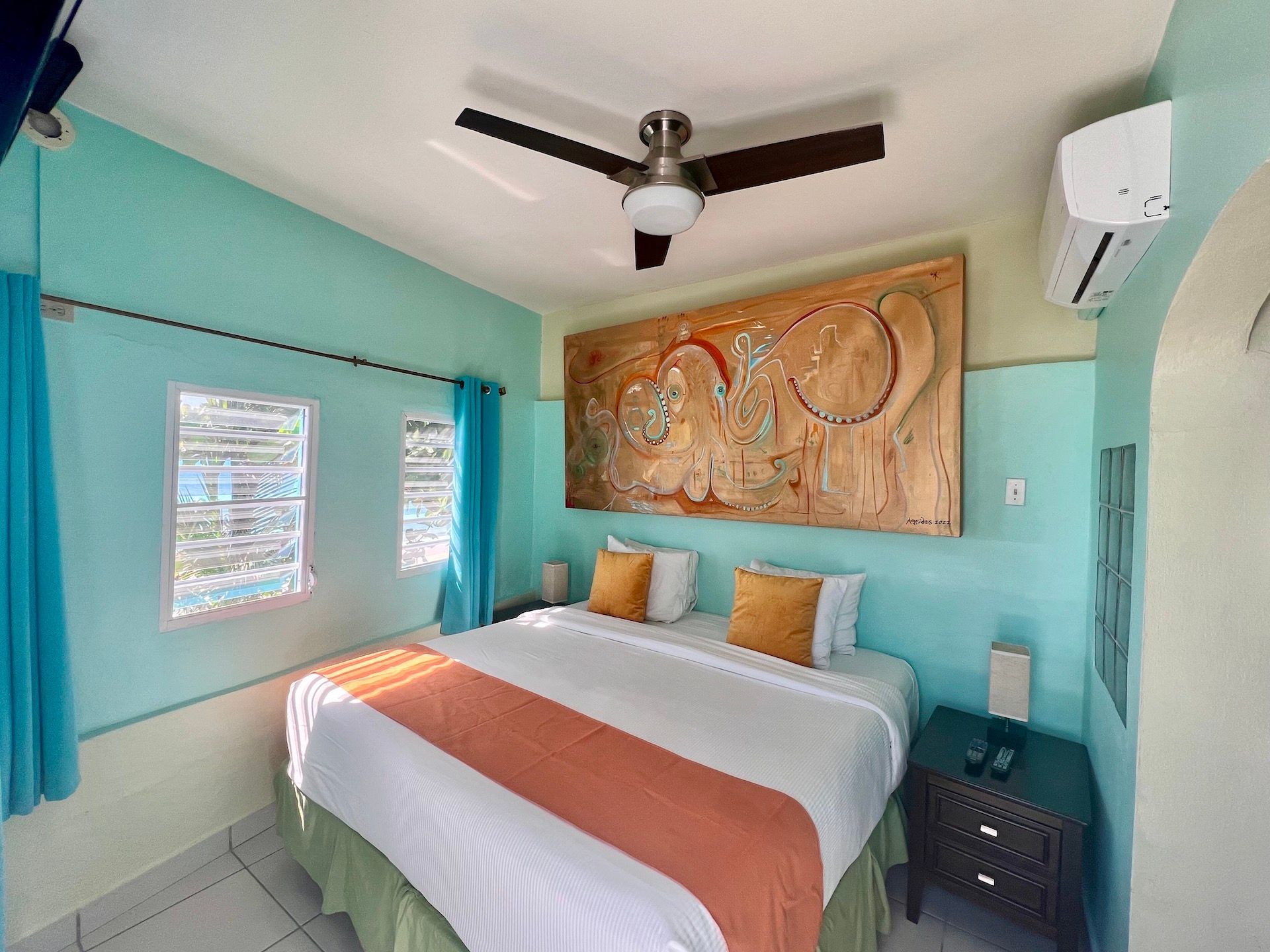 Bedroom with a king-size bed, teal walls, orange accents, and a large wooden artwork.