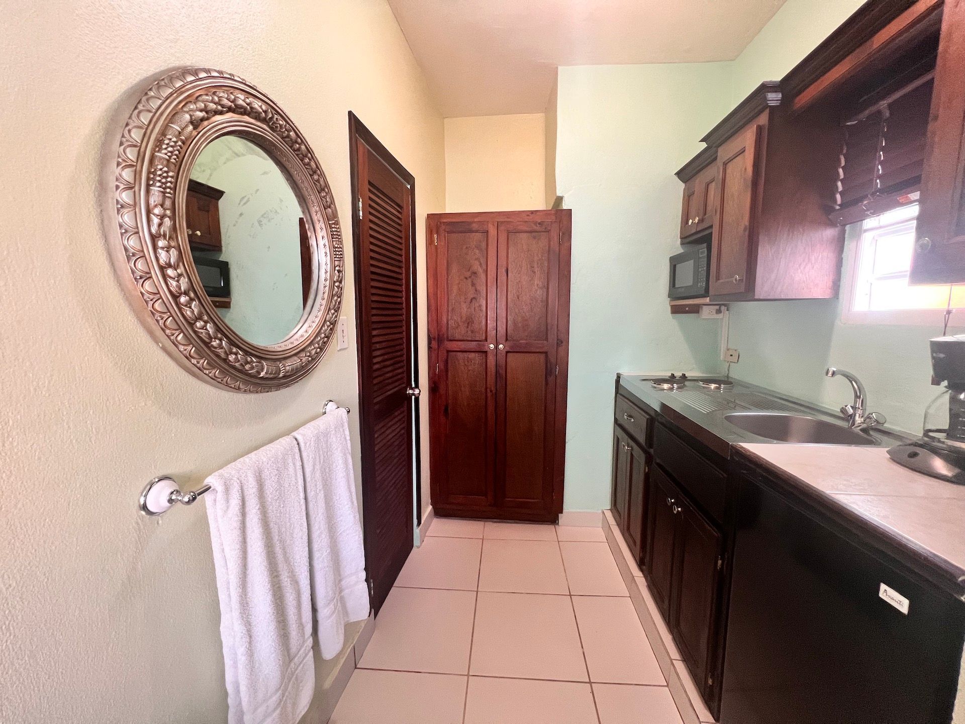 Narrow kitchen with dark cabinets, mirror, towel rack, and wooden pantry.