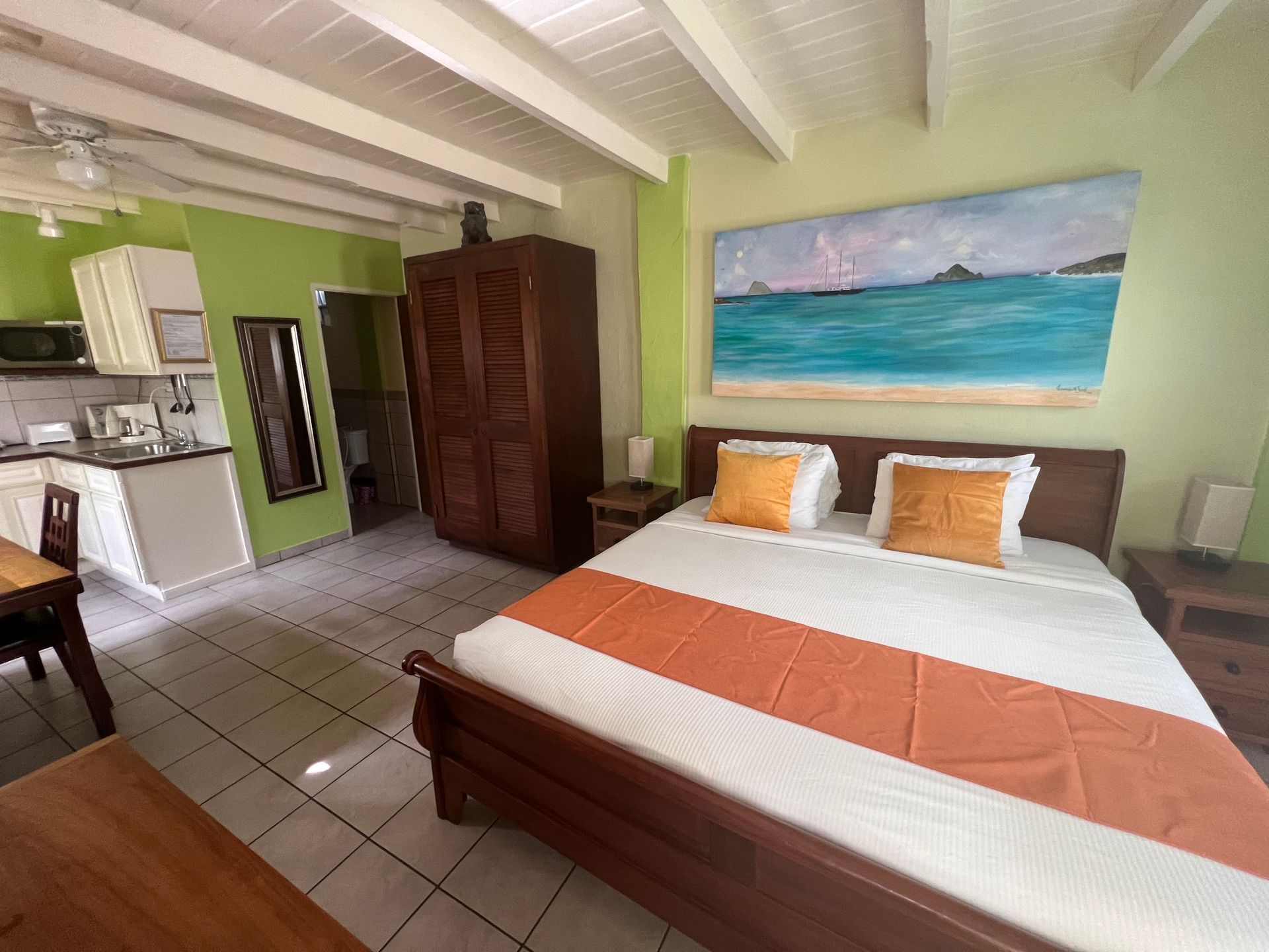 Bedroom with bed, wardrobe, kitchenette, green walls, and ocean painting.