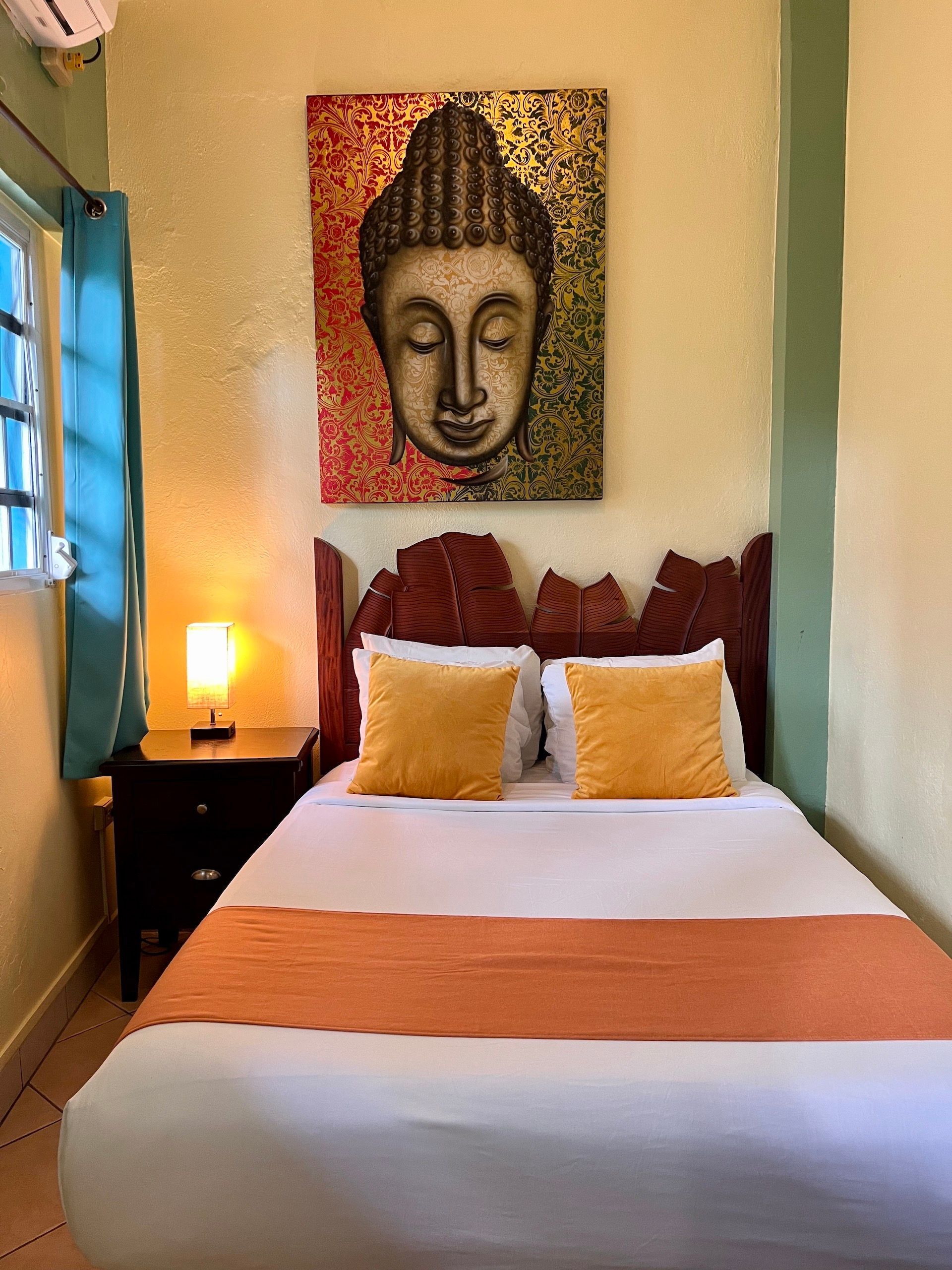 Bedroom with a bed, nightstand, and Buddha art; mustard and orange accents.
