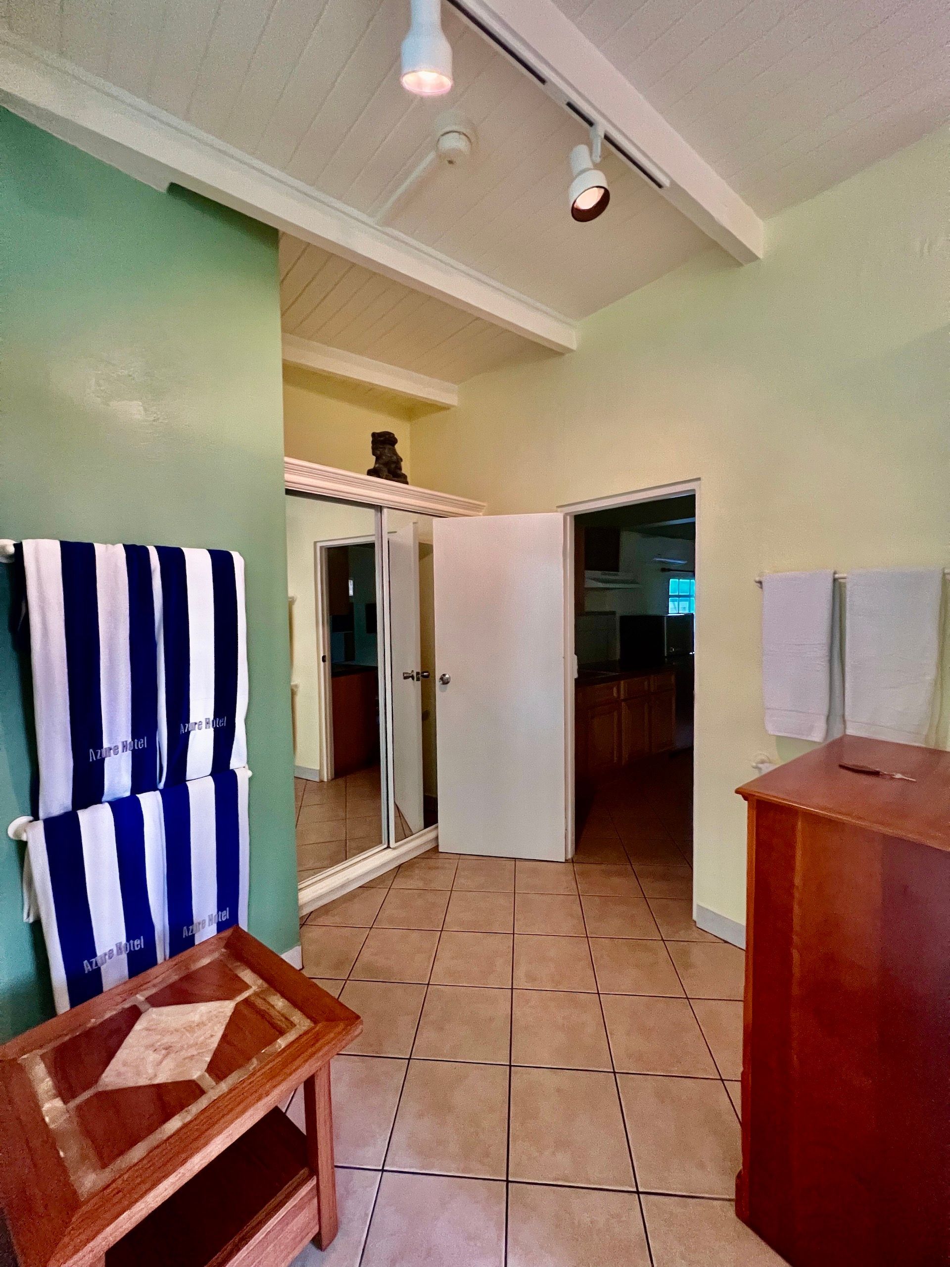 Hallway with open door, towels, small wooden table, light green walls, and tile flooring.