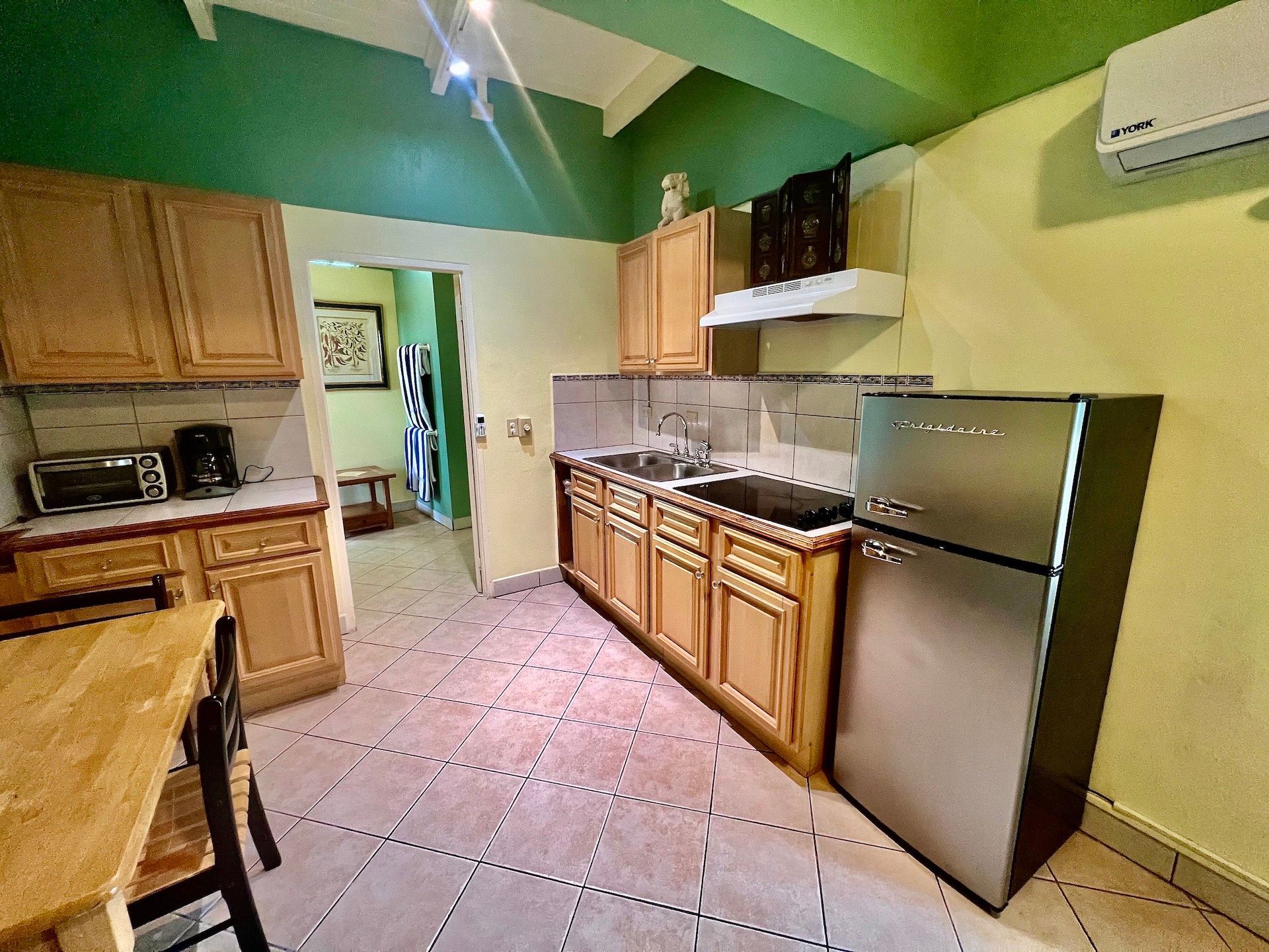 Kitchen with light wood cabinets, stainless steel refrigerator, tile floor, and green walls.