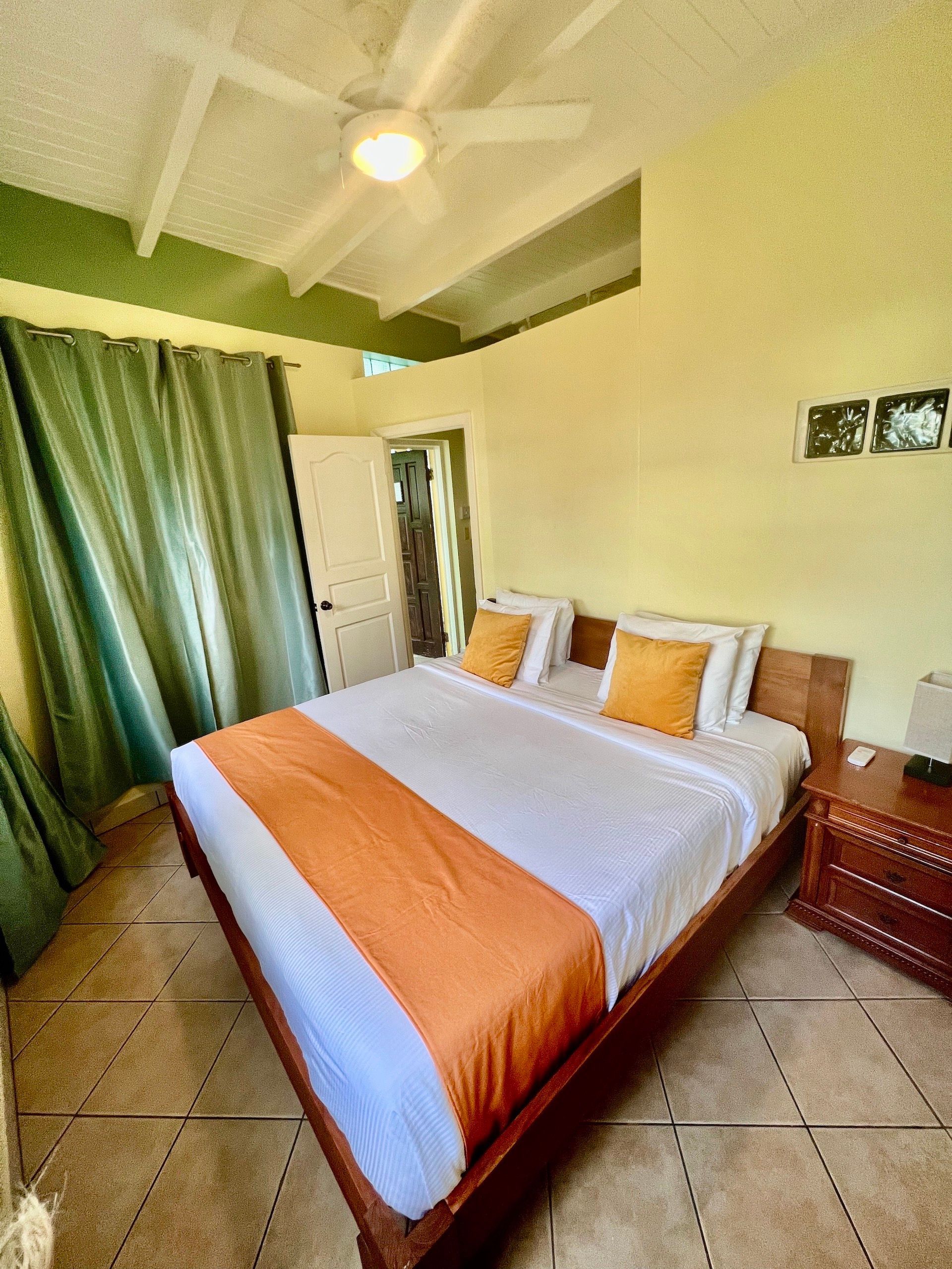 Bedroom with a queen-sized bed, orange accents, and green curtains.