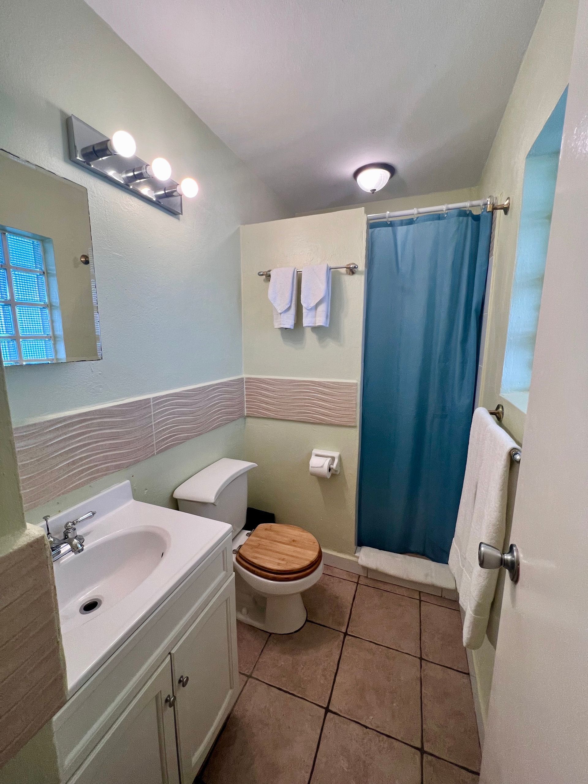 Small bathroom with white vanity and toilet, brown tile, green walls, and a blue shower curtain.