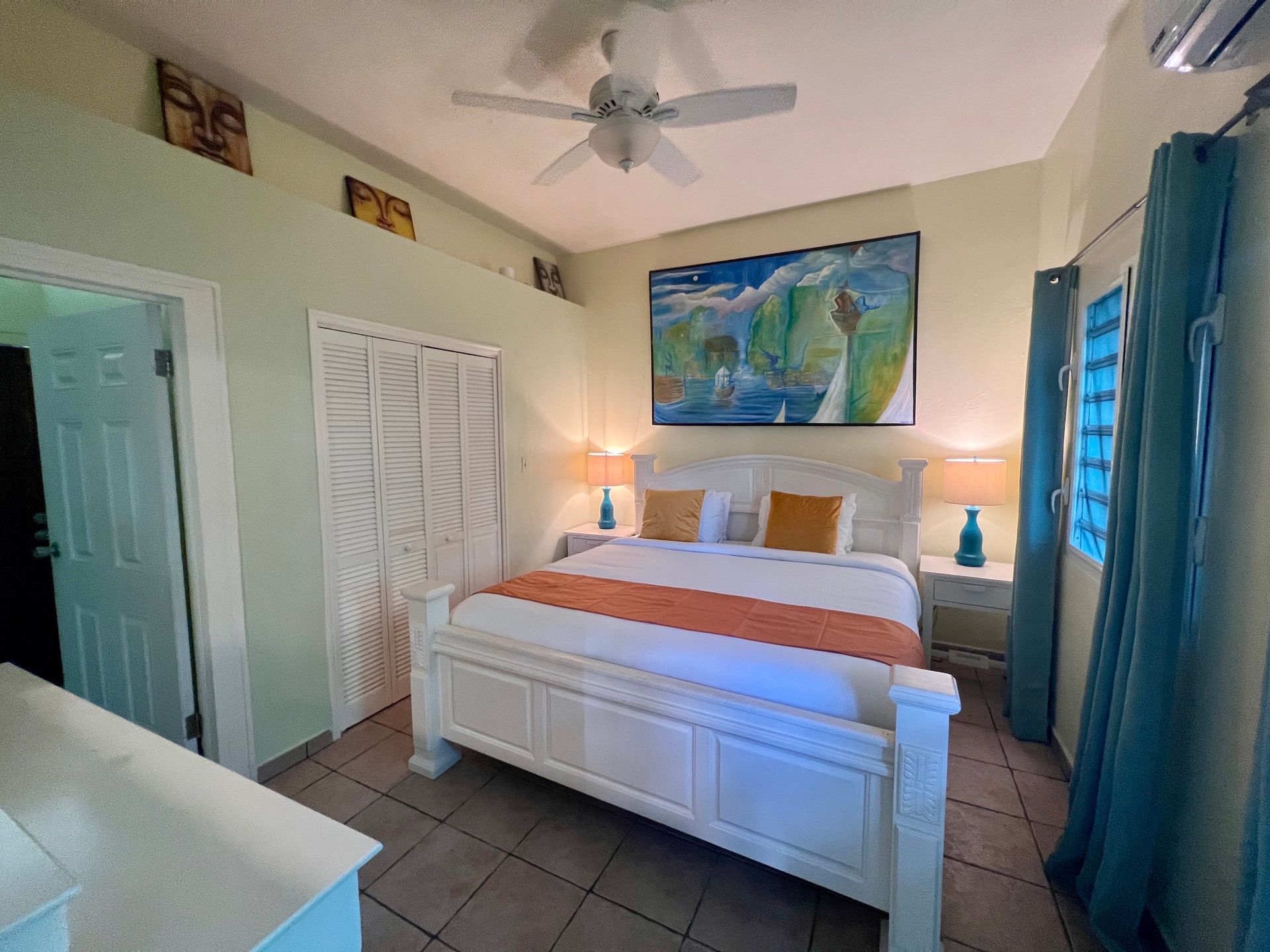 Bedroom with white bed, orange runner, and large landscape painting; light blue curtains.