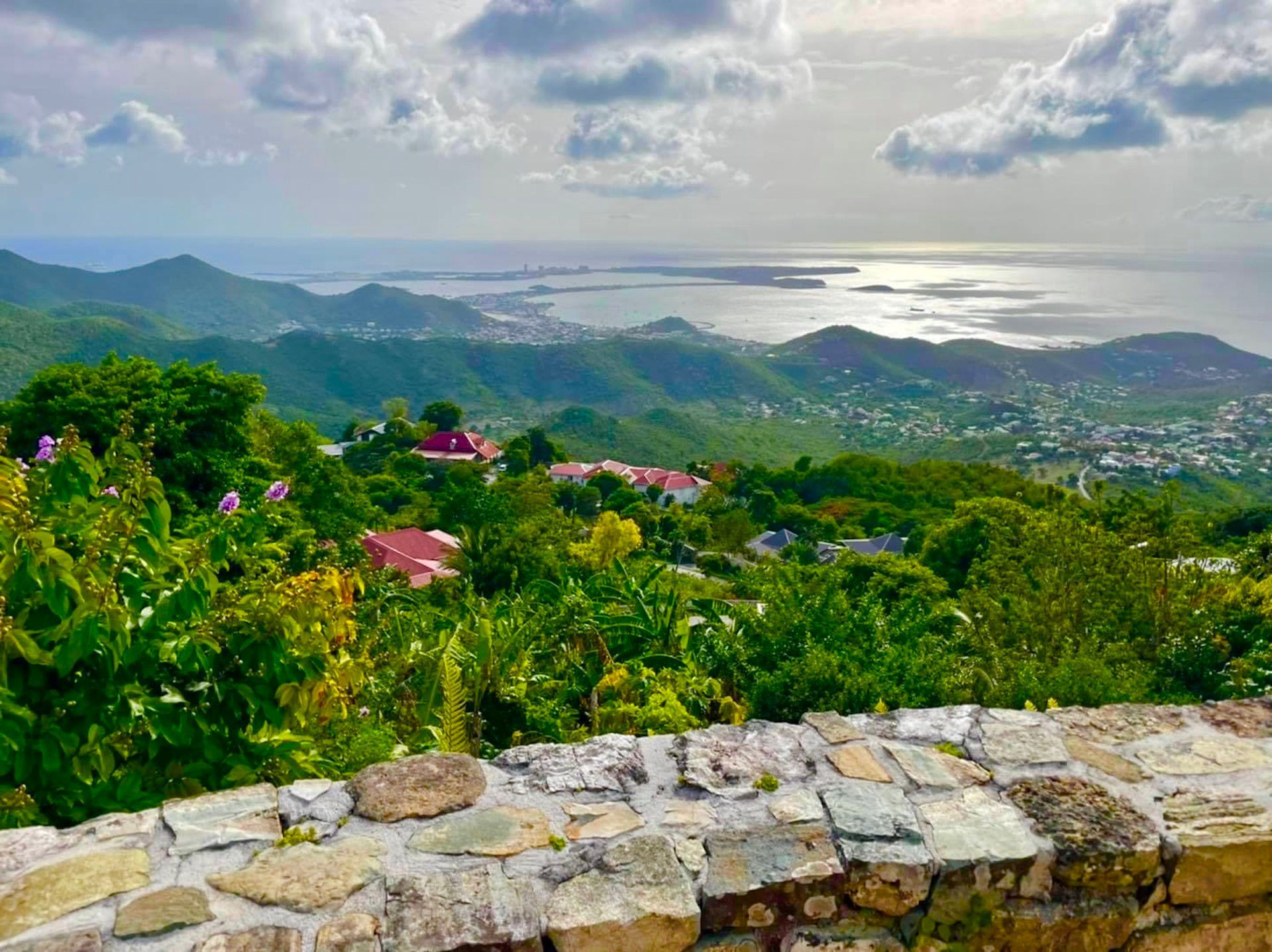 Scenic view of green hills, buildings, and ocean under a cloudy sky.