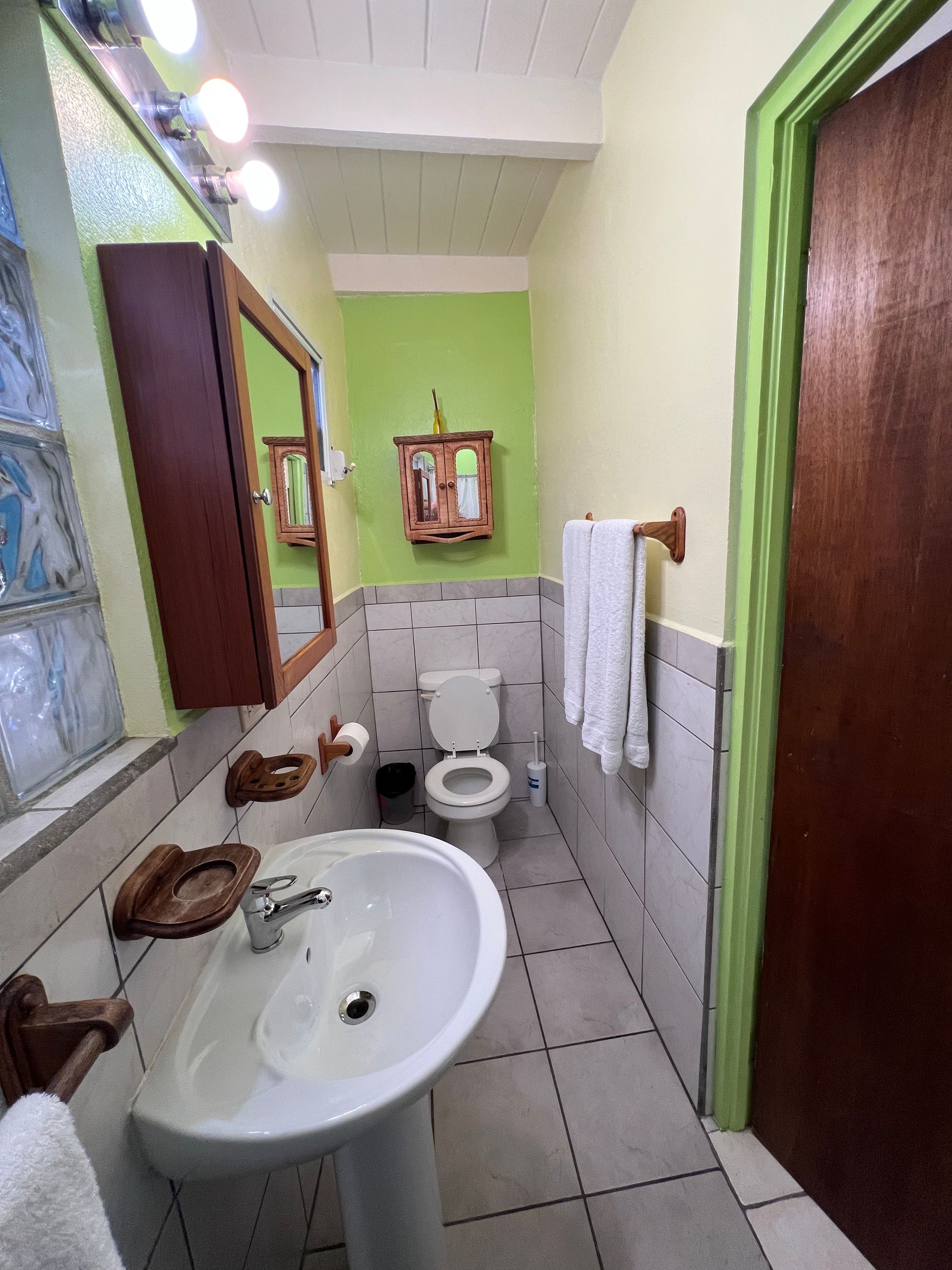 Bathroom with a white sink, toilet, and towels; walls are green and beige.