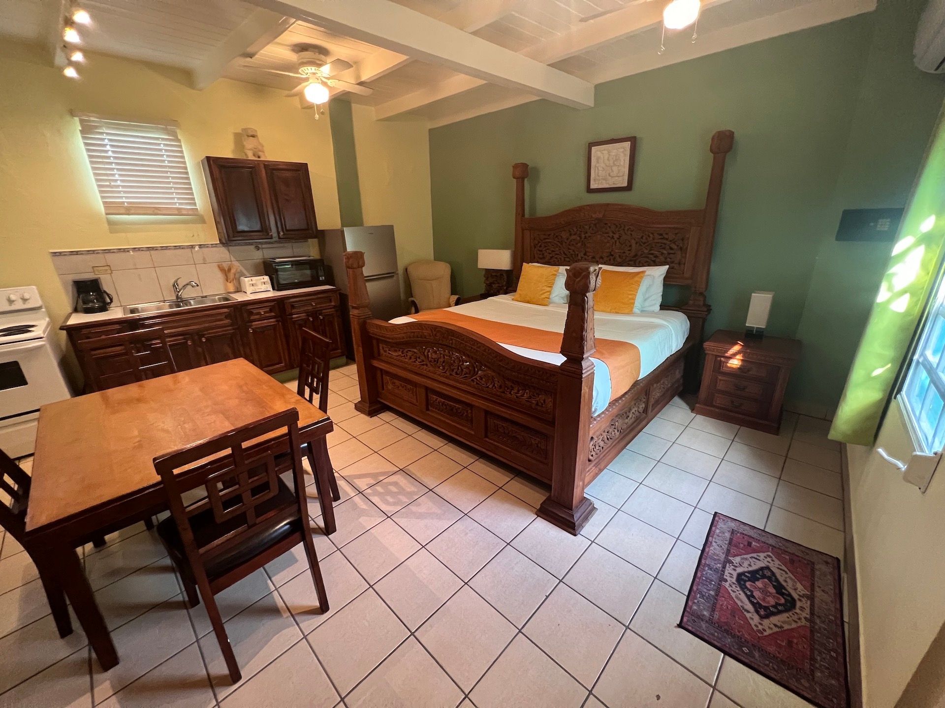 Bedroom with a dark wooden bed, dining table, kitchenette, and green walls.