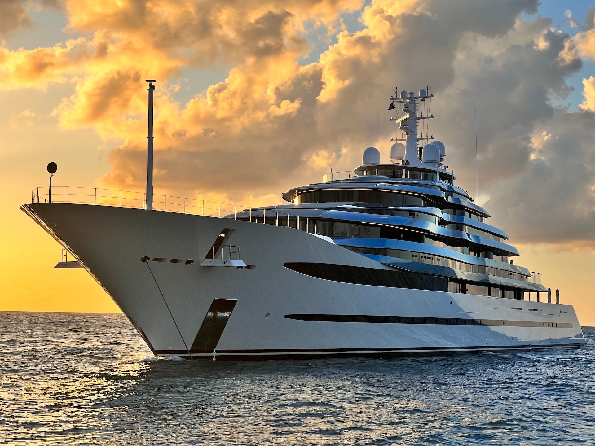 Luxury yacht sailing on ocean at sunset.