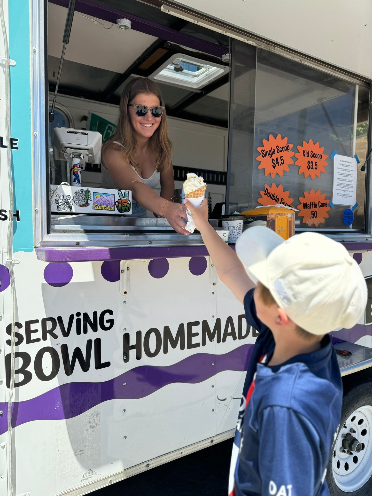A boy is reaching for an ice cream cone in front of a serving bowl homemade food truck.