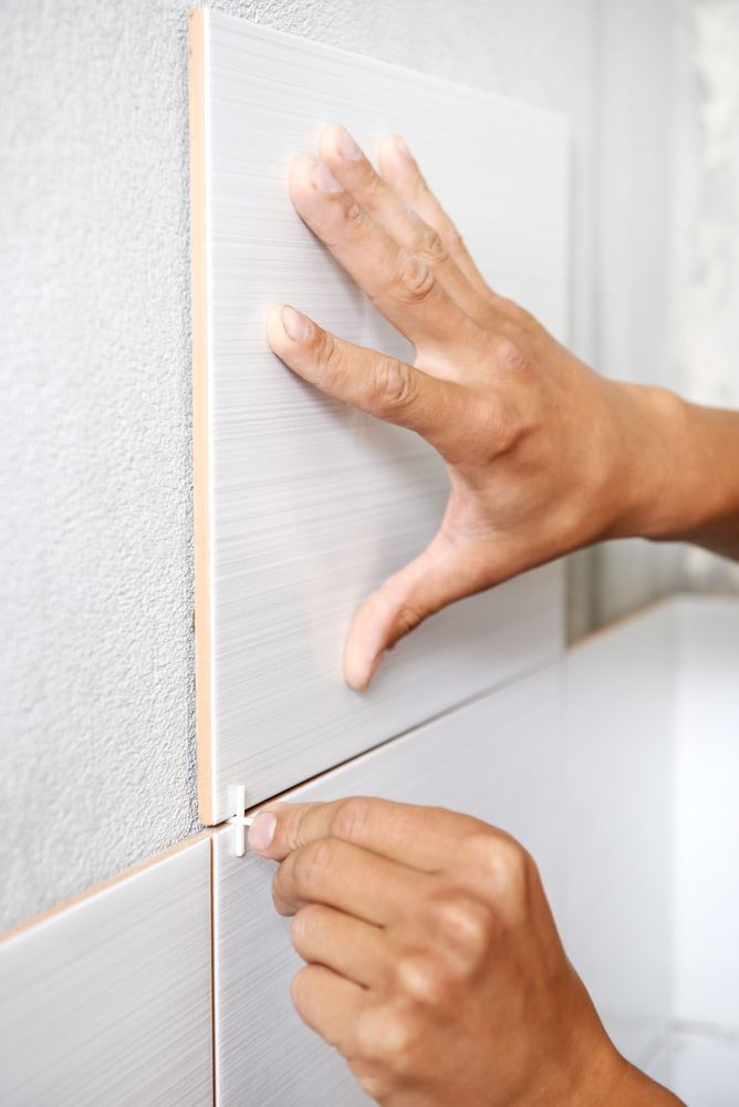 Hands Installing a Light-coloured Tile on a Wall — Tropic Tiling in Yungaburra, QLD