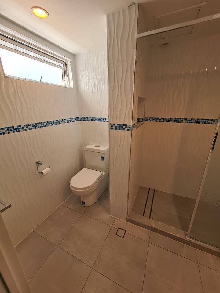 Bathroom With White Walls, Toilet, Shower, and Window — Tropic Tiling in Malanda, QLD