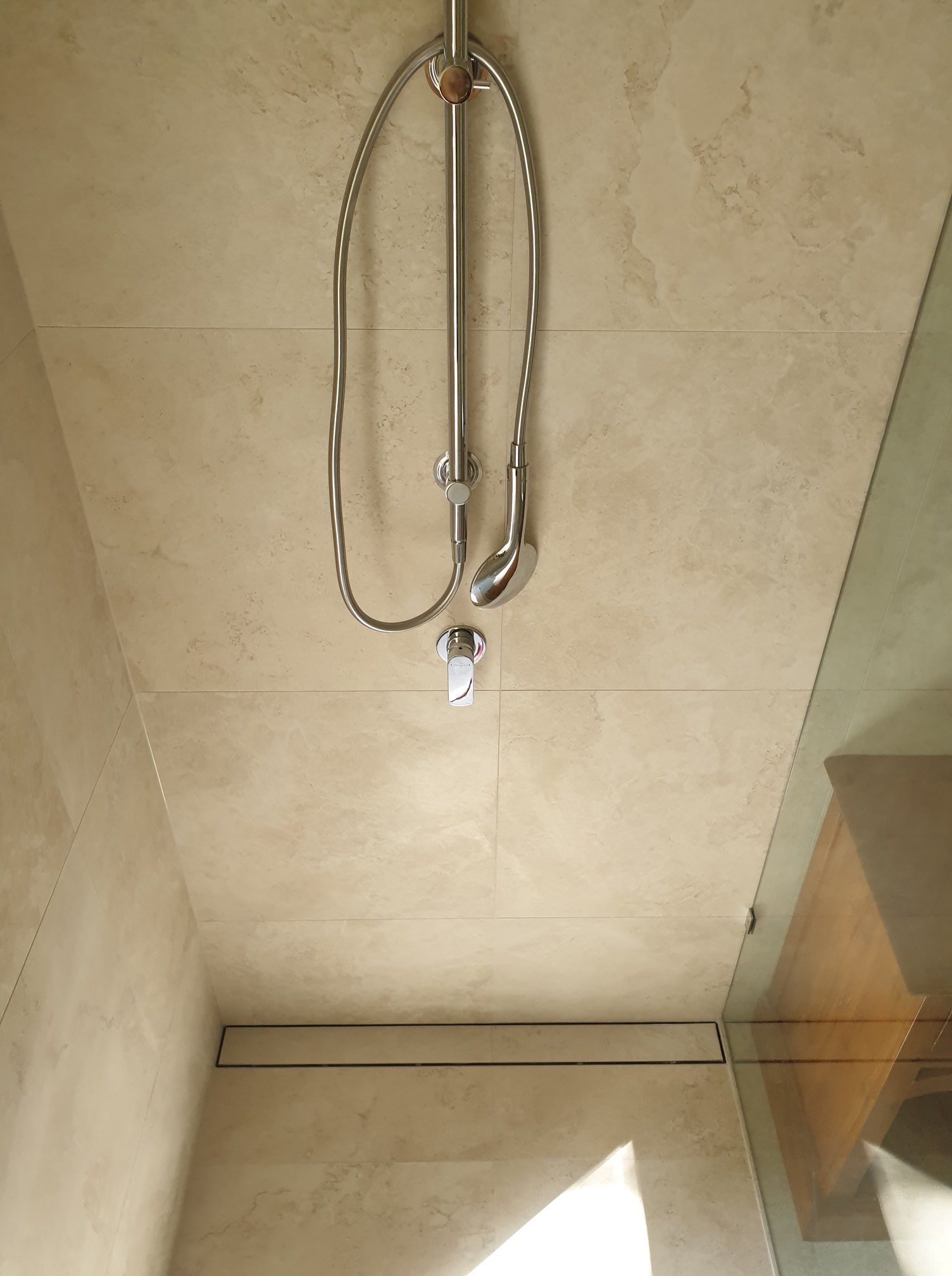 Showerhead and fixtures mounted on beige tiled wall, glass shower door visible — Tropic Tiling in Tolga, QLD