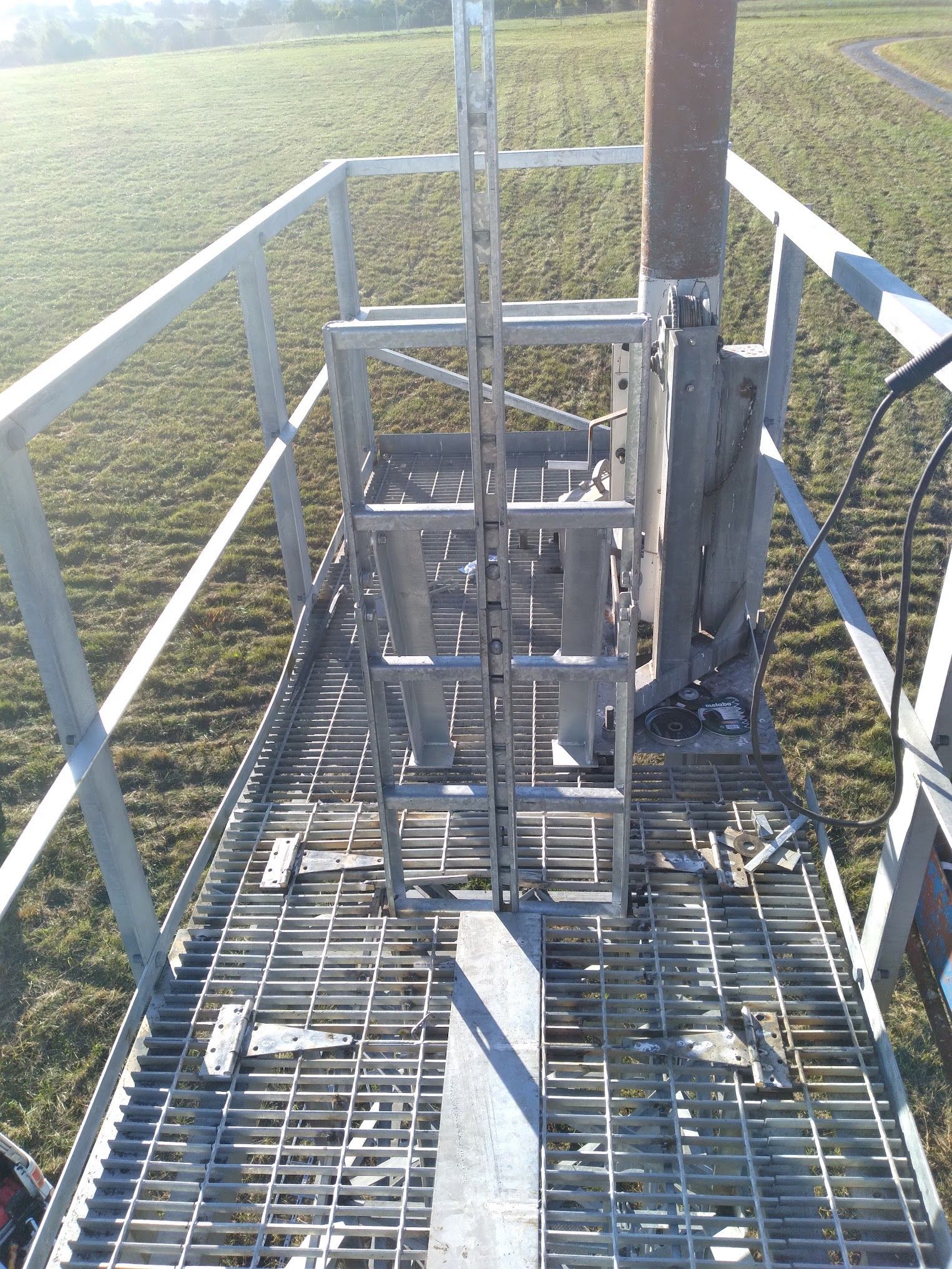 A metal platform with stairs leading up to a pole in a field.