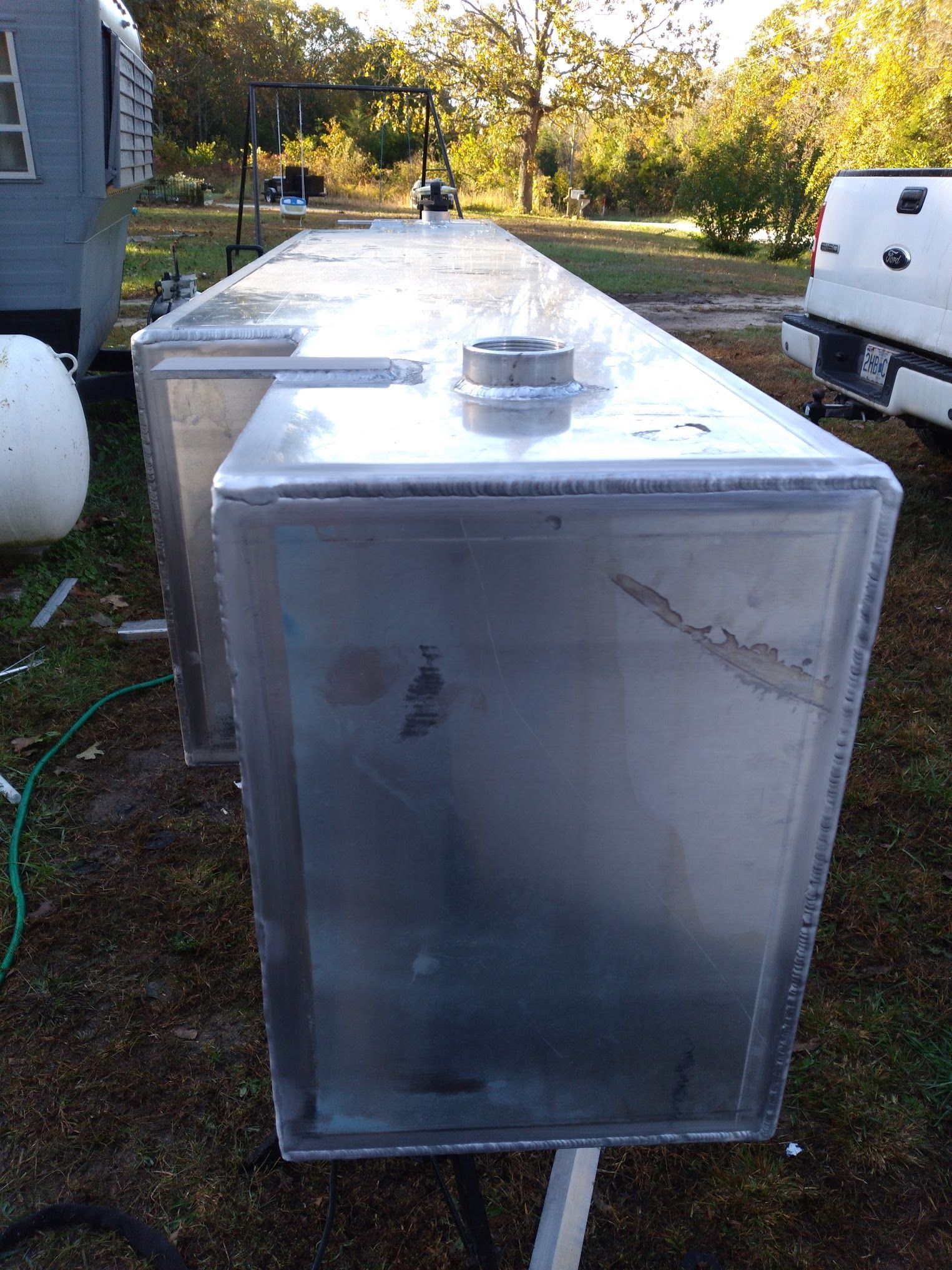 A large aluminum tank is sitting in the grass next to a truck.