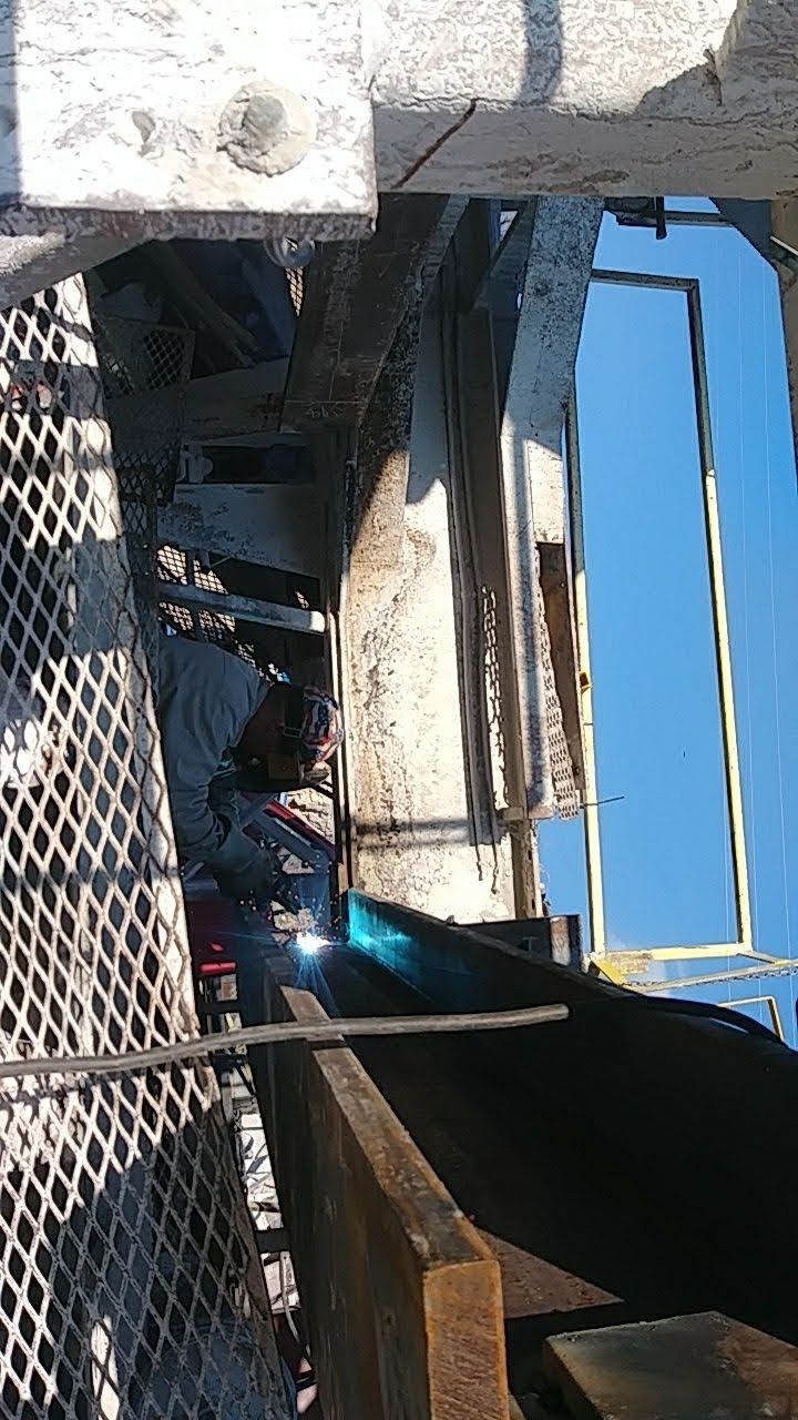A man is welding a metal structure with a blue sky in the background.