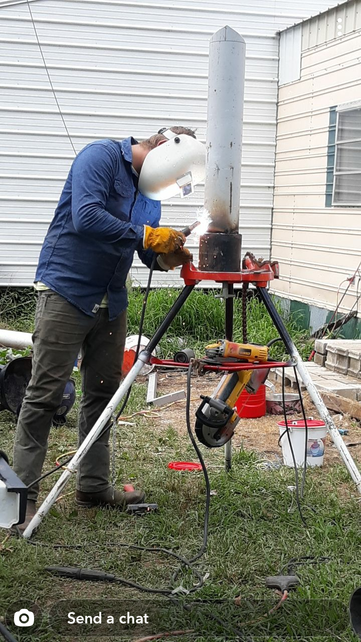 A man is welding a pipe on a tripod in front of a house.