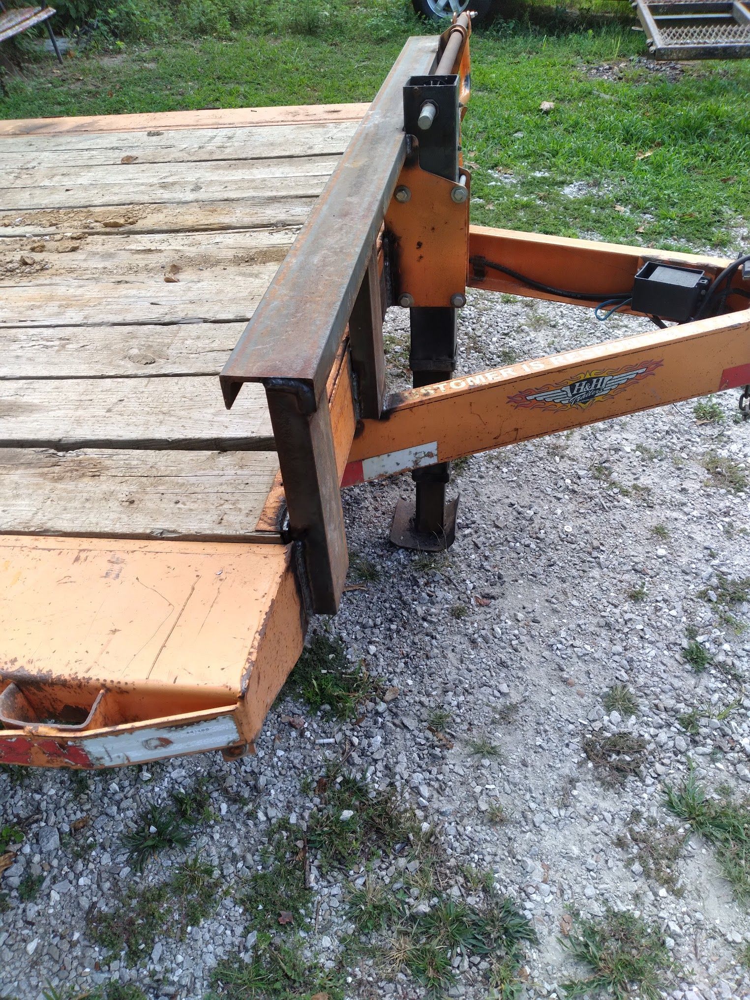 A wooden trailer is sitting on top of a gravel road.