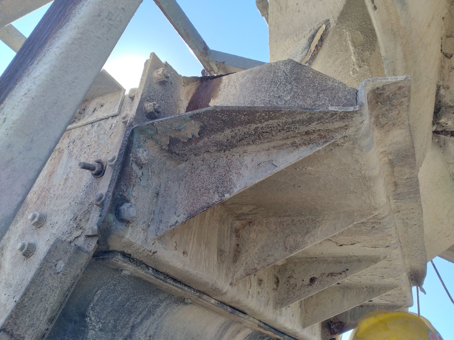 A person wearing a yellow hard hat is standing next to a concrete structure.