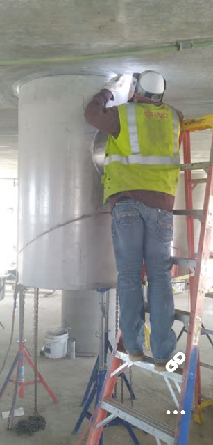 A man is standing on a ladder welding a pipe.
