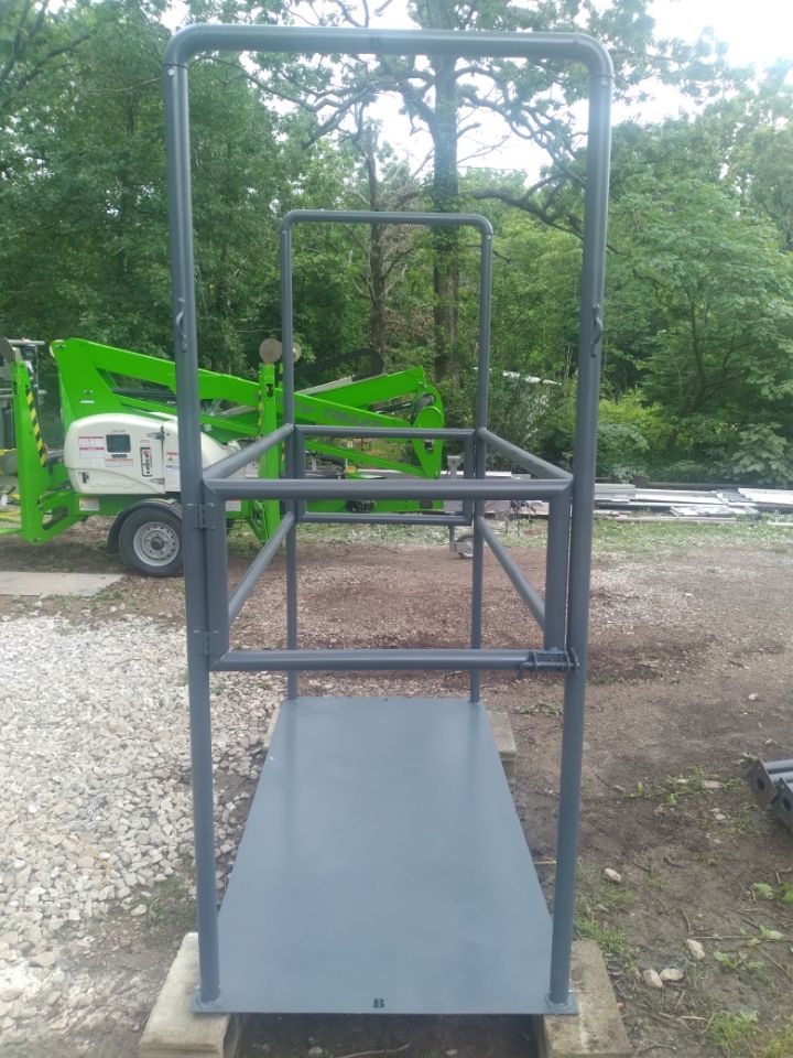 A metal platform is sitting in front of a green crane.