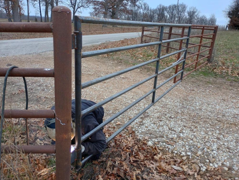 A rusty metal gate is open to a gravel road