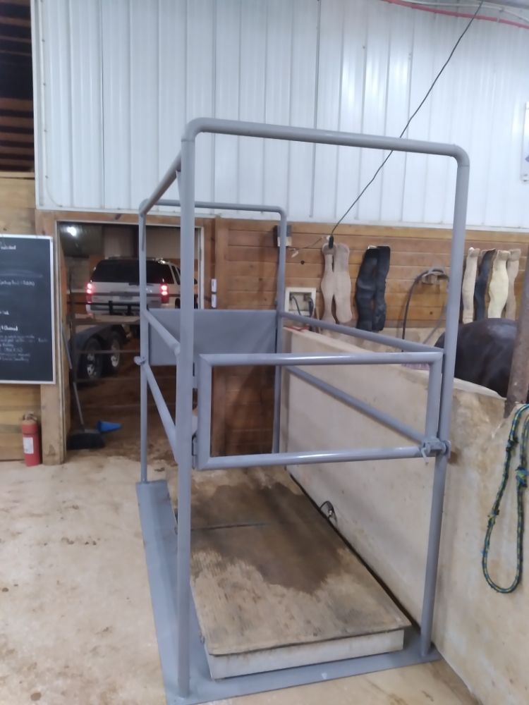 A horse weighing scale in a stable with a car in the background