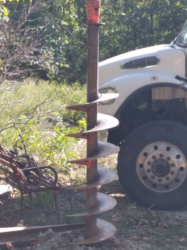 A white truck is parked next to a large drill bit