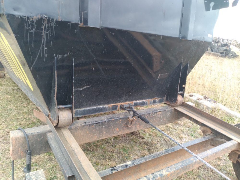 A dumpster is sitting on top of a trailer in a field.