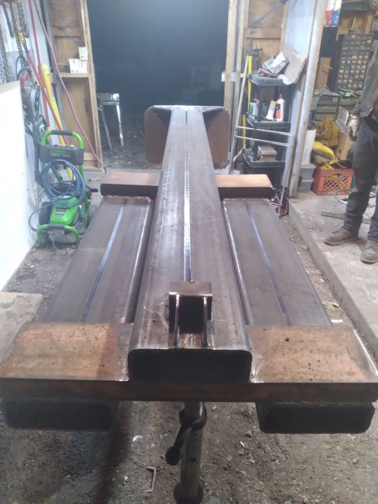 A long wooden table is sitting in a garage next to a green lawn mower.